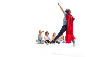 Power. Child pretending to be a superhero with his friends sitting around him. Kids excited, inspired by their strong friend in red coat isolated on white background. Dreams, emotions concept.