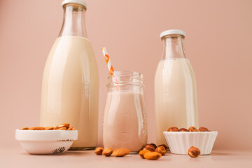 Various vegan plant based milk and ingredients. Dairy free milk substitute drinks on pink background, closeup view