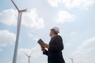 Engineer windmills are working on tablet PC with the wind turbine in background