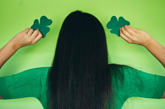 Modern girl holding a shamrock on an isolated green background. Happy St Patrick's day. Focus on hair.