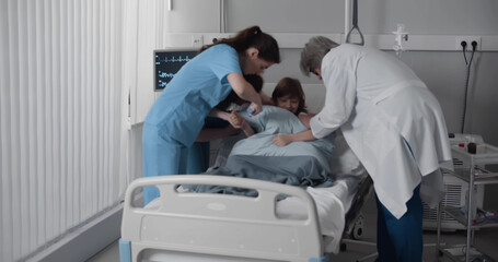 Medical team checking up preteen boy lying in hospital bed