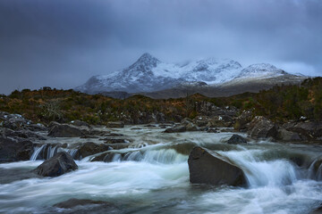 Fototapeta na wymiar Dramatic sky over large mountains from the River Sligachan on the Isle of Skye Scotland with the Cuillin mountain range in the distance with snow in winter, Isle of Skye, Scotland