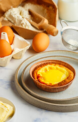 Egg tart, traditional Portuguese dessert, pastel de nata in a gray plate on a marble background . Portuguese puff and ingredients for cooking (flour, butter, eggs, milk). Selective focus