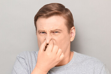 Portrait of mature man pinching his nose and grimacing from disgust