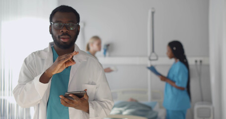 African man doctor looking at camera and talking with colleagues treating patient on background