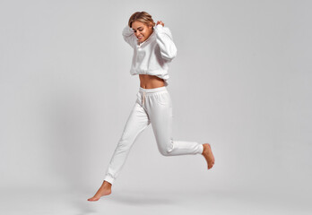 Fototapeta na wymiar Beautiful blonde woman jumping in the air in white tracksuit isolated on gray background
