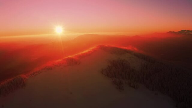 Flying above Winter mountain. During Sunrise or Sunset. Red, magenta colored Sky. Flying above Clouds. Covered with Snow. Shining Morning Sun. Beautiful Landscape 