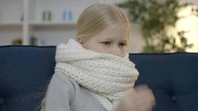 Unhappy little girl in scarf coughing and feeling sick, suffering from flu