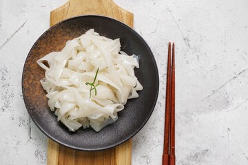 Grainy look Fresh Kwetiau as White Chinese noodles made from Rice in black plate. Popular in South East Asia on texture white background