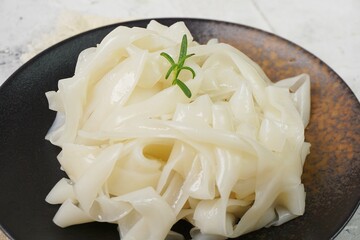 Grainy look Fresh Kwetiau as White Chinese noodles made from Rice in black plate. Popular in South East Asia on texture white background. Selective focus