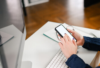 cropped shot of a young woman working from home using smart phone and computer, woman's hands using smart phone in interior, woman at home workplace using technology,
