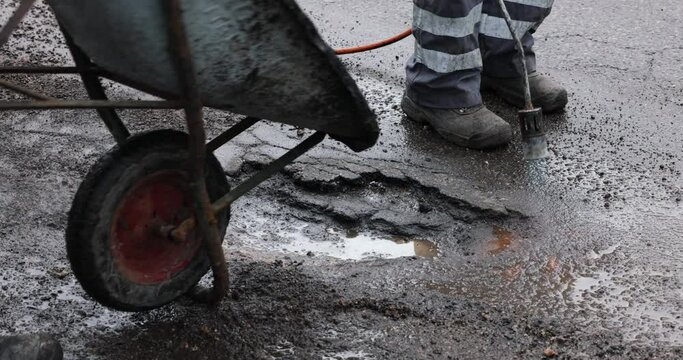 workers repairing pothole with bitumen asphalt on the road