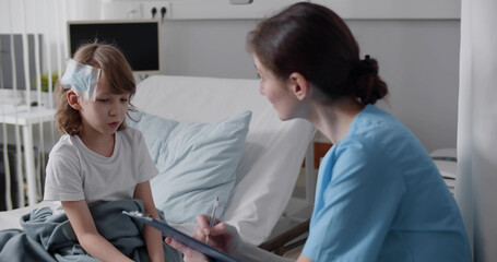 Fototapeta na wymiar Woman pediatrician writing diagnosis on clipboard near kid with bandaged head sitting in bed