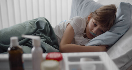 Obraz premium Sick preteen boy with nasal tube lying in hospital bed looking at tray with medication