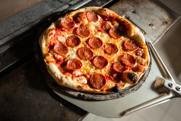 freshly made pepperoni pizza, coming out of the oven of a pizzeria with shovel.