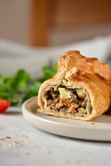 English pie with minced meat and vegetables, cutaway on a gray plate.