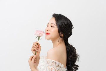 Attractive elegant Asian woman holding flower and wearing white dress over white background.