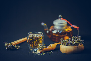 Thyme leaves in wooden bowl and bamboo spoon.  Tea cup and teapot with thyme flower on black...