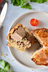A slice of English pie with minced meat and meat, and part of the pie, made from shortcrust pastry, lies on a gray plate, top view.
