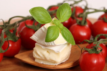 Zwei Stücke Camembert mit Holzlöffel auf einem Holzbrett und Tomaten, Basilikum