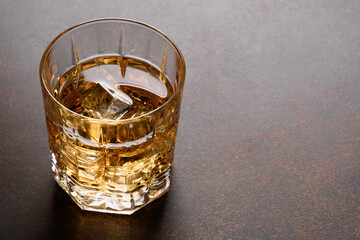 Glass of cold whiskey on dark brown background. Close up.