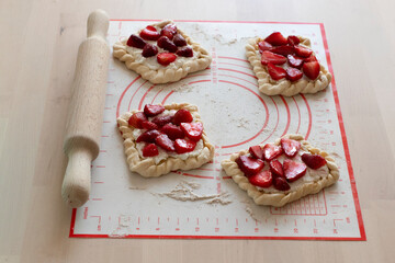 homemade food, buns with cottage cheese and strawberry slices, laid out on a silicone mat with flour. Baking before cooking, eating at home, baking recipes. cook at home