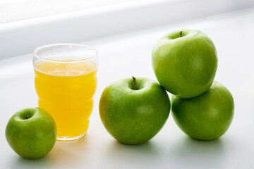 Ripe green apples and apple juice on a white window. Juicy fruit and juice on a white background.