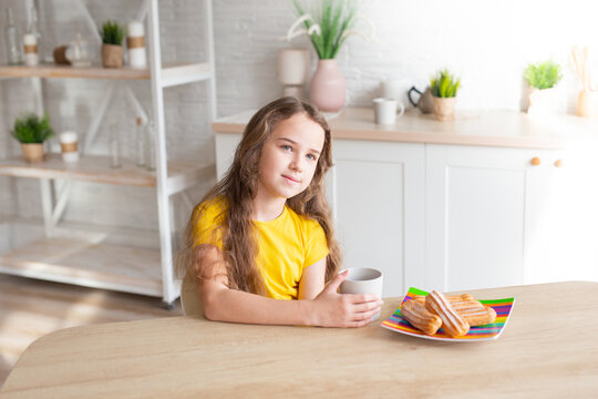 cute school-age girl with curly-haired girls sits at a table in the kitchen, has fun, singing while waiting for food, a delighted child relaxes at the counter, enjoys a happy childhood at home 
