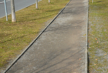 gravel road in the city park light sand, green lawn and tree trunks in the alley, straight narrow,...