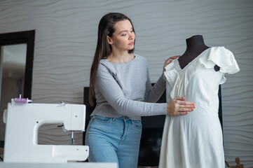 Caucasian woman sews a dress at home. Workspace of a seamstress