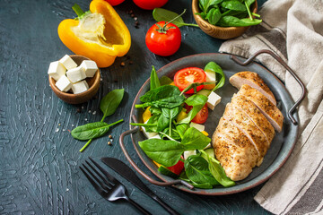 Healthy food. Ketogenic diet lunch. Grilled chicken fillet with fresh vegetable salad, spinach and feta on a dark stone background. Copy space.
