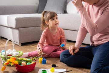 Naklejka premium A mother and her daughter painting Easter eggs at home.