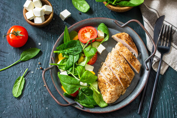 Healthy food. Ketogenic diet lunch. Grilled chicken fillet with fresh vegetable salad, spinach and feta on a dark stone background.