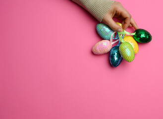 female hand holding multicolored decorative easter eggs on pink background