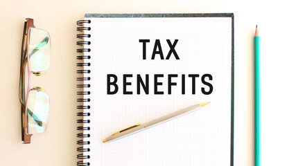 Notepad with text TAX BENEFITS on a white background, near glasses and pencil.