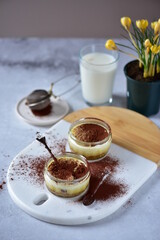 Cheesecake in jars on a white marble board with spoons in a row, on a gray background, in the background a glass of milk and a pot with yellow crocuses.