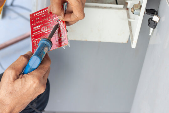 The Hands Of A Mechanic Holding A Soldering Iron And Lead To Fix The Vending Machine.