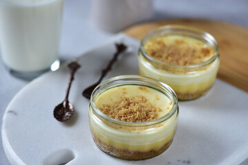 Cheesecake in jars on a white marble board with spoons next to it.