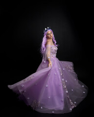 Full length portrait of girl wearing long purple fantasy ball gown with crown and pink hair, standing pose with elegant gestural  movements against a studio background.