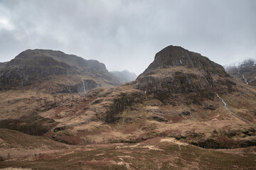 Majestic moody landscape image of Three Sisters in Glencoe in Scottish Highlands on a wet Winter day wit high water running down mountains