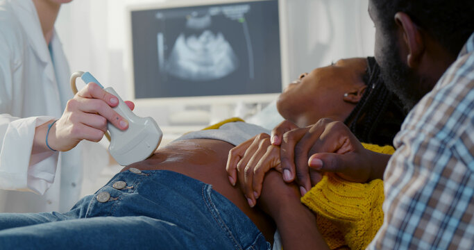 Afro pregnant couple smiling looking at sonogram results on monitor while on checkup at gynecologist