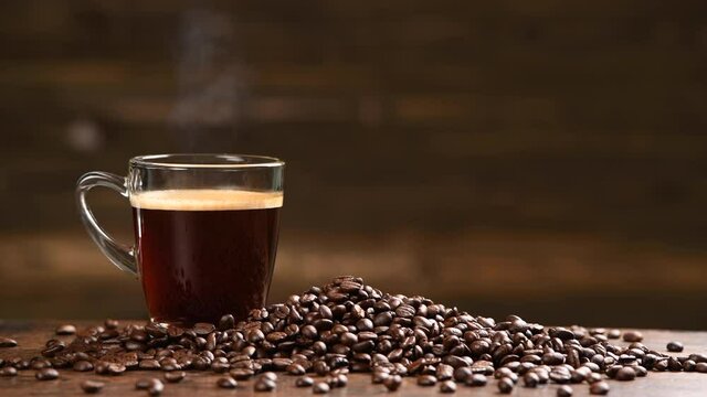 Cup glass of coffee with smoke and coffee beans on burlap sack on old wooden background