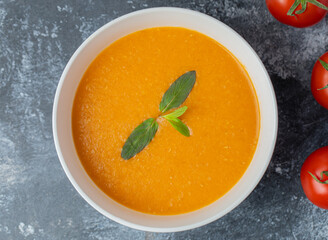 Delicious colored tomato cream-soup with herbs on grey background