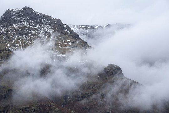 Epic Winter landscape image of view from Side Pike towards Langdale pikes with low level clouds on mountain tops and moody mist swirling around © veneratio