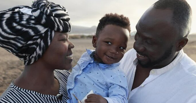 Happy african family having fun on the beach - Mother, father and little son looking in camera and smiling - Love and people lifestyle concept