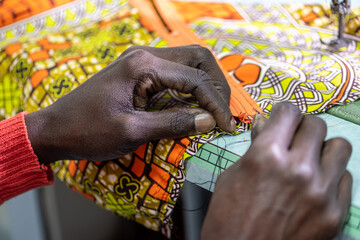 close up of hands of african tailor working, craftman making dress with traditional wax fabric from...
