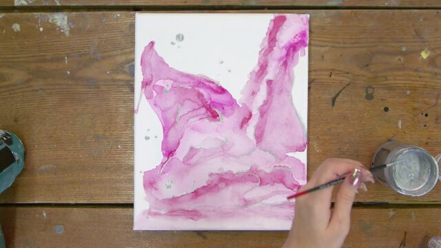 Fluid Art. Abstract pink painting. Top view of female artist uses paintbrush and silver paint to draw an abstract picture