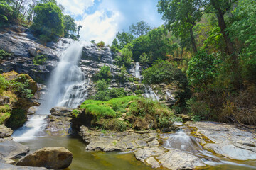 Obraz premium The waterfall is surrounded by beautiful trees and rocks.