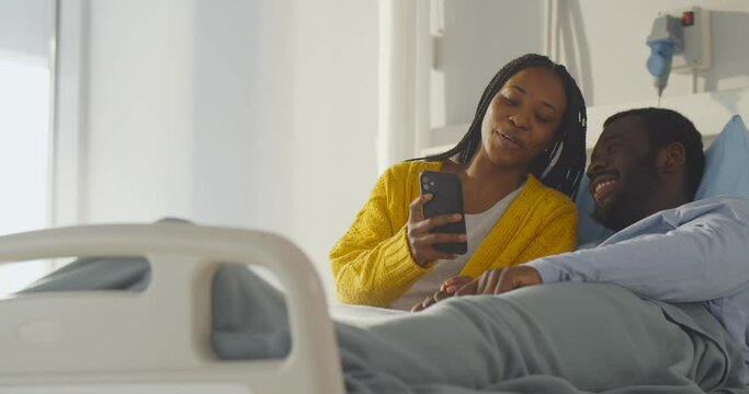 African couple resting in hospital bed and using smartphone together