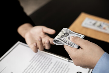 Business men fold the dollar bills and give them to their business partners to bribe an upcoming project, bribery is an illegal and bad practice. The concept of corruption.